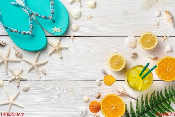 colorful summer background. cocktail with ice, oranges, lemons, shells, starfish and flip flops on a light wooden background.