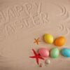 colorful eggs and text happy easter written on sand