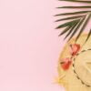 ladies straw hat, sunglasses and palm leaf on pink background wi