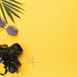 photo camera, sunglasses, starfish and palm leaf on a yellow bac