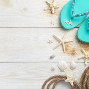 sea background with seashells, rope and summer flip flops on a white wooden background.