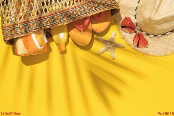 straw bag with beach holiday accessories on yellow background an