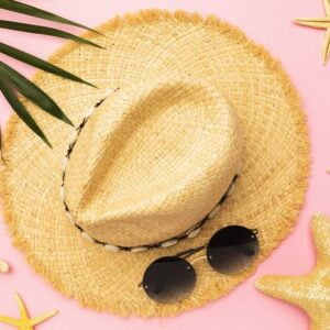 womens straw hat, sunglasses, starfish and palm leaf on a pink b