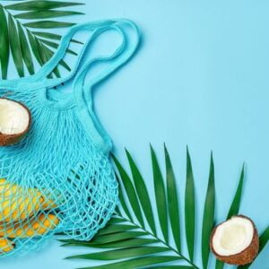 zero waste mesh bag with bananas and coconut on bright blue background. top view, copy space.