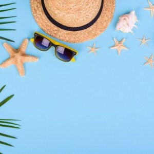 beach accessories: glasses and hat with shells and sea stars on a colored background