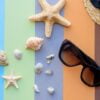 beach accessories: glasses and hat with shells and sea stars on a colored background