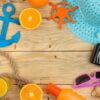 summer accessories. beach accessories. hat, sunscreen, sunglasses, camera, and orange on a natural wooden table. top view. space for text