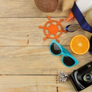 summer accessories. beach accessories. hat, sunscreen, sunglasses, camera, and orange on a natural wooden table. top view. space for text