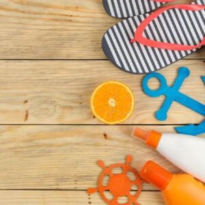 summer accessories. beach accessories. sunscreen, flip flops, and orange on a natural wooden table. top view. free place