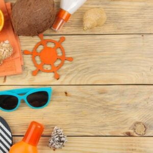 summer accessories. beach accessories. sunscreens, sunglasses, flip flops, and an orange on a natural wooden table. top view. free place