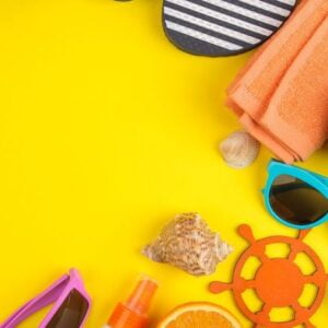 summer accessories with shells, sun glasses, orange and coconut on a bright yellow background. top view. space for text