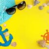 summer accessories with sun glasses, a hat and shells, on a bright yellow background. top view. space for text