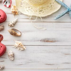 summer background concept: crocs, starfish, seashells, straw hat on light wooden surface