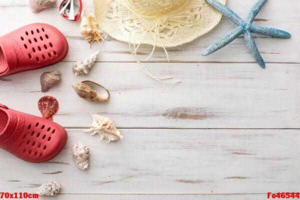 summer background concept: crocs, starfish, seashells, straw hat on light wooden surface