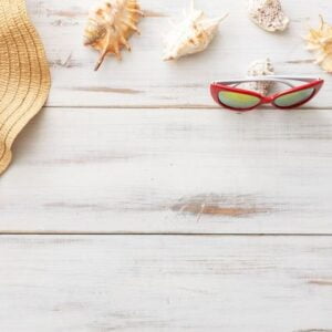 summer background concept: straw hat, seashells, sunglasses on light wooden surface