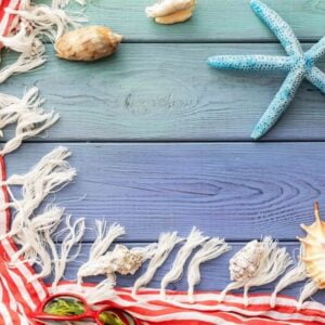 summer background: fringed pareos, seashells, sun goggles, starfish on a blue wooden background