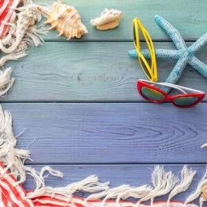 summer background: fringed pareos, seashells, sun goggles, starfish on a blue wooden background
