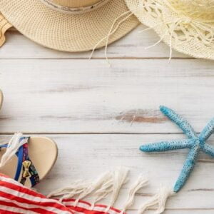 summer background: straw hat, sandals, fringed pareo on a light wooden background