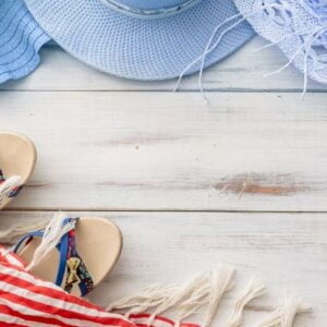 summer background: straw hat, sandals, fringed pareo on a light wooden background