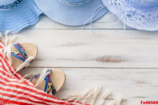 summer background: straw hat, sandals, fringed pareo on a light wooden background