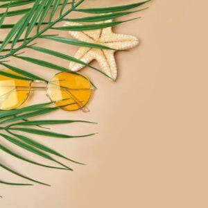 sunglasses and palm leaves top view on beige background