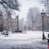 a snowy city square with a fountain and benches